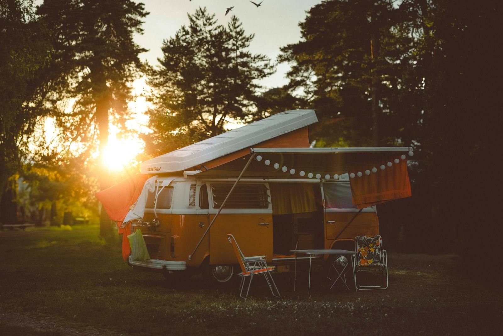 Combi aménagé garé sous les pins au soleil couchant, auvent déplié et guirlande lumineuse