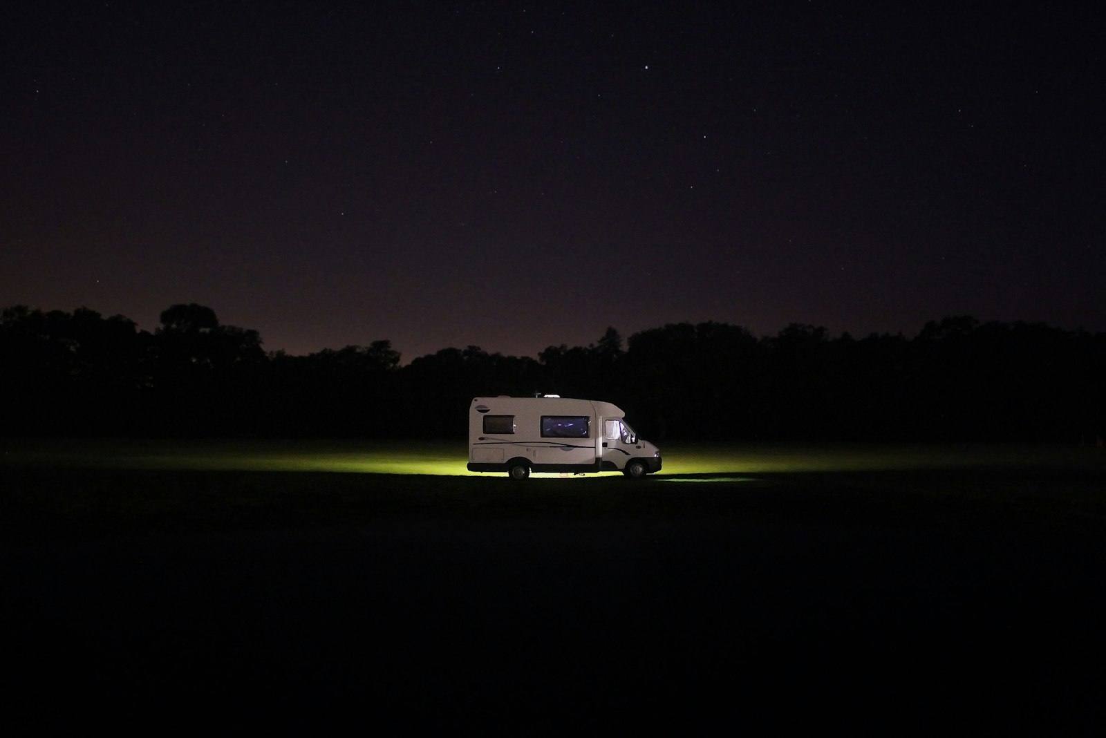 Camping-car éclairé, seul au milieu d’un champ plongé dans la nuit