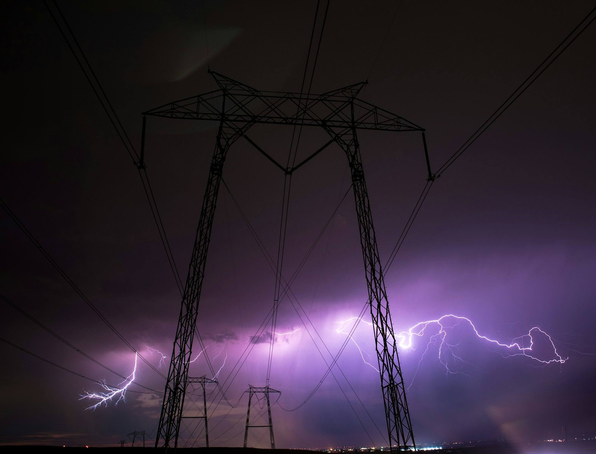 Éclairs violets derrière un pylône électrique photographié depuis le sol, la nuit