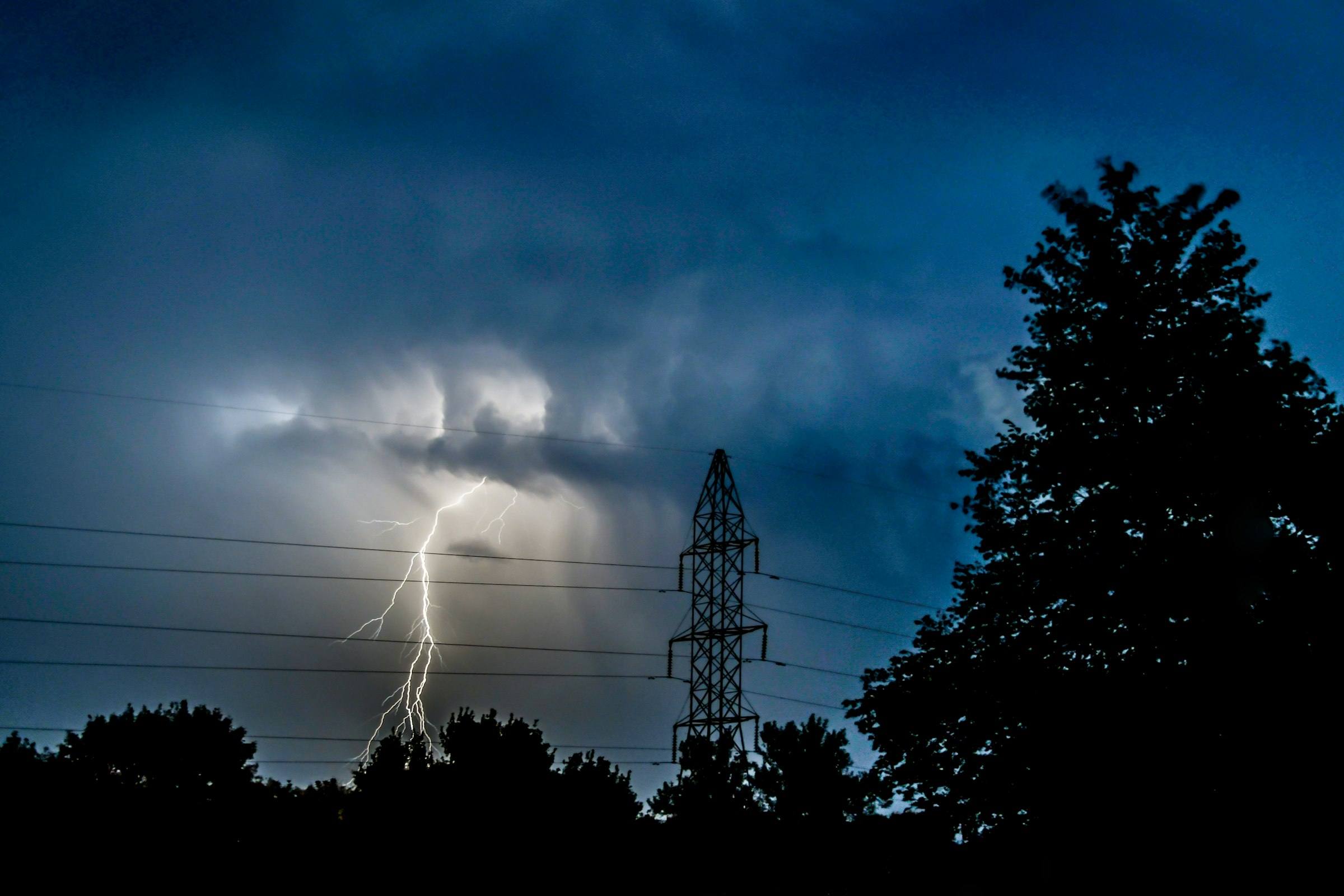Éclair tombant près d’un pylône haute tension, sous un ciel d’orage bleu nuit