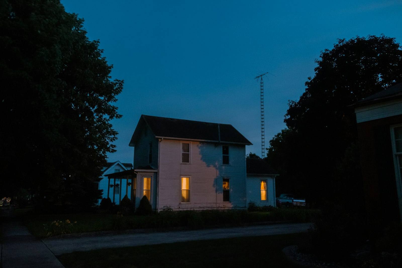 Maison à étage aux fenêtres éclairées, à la tombée de la nuit
